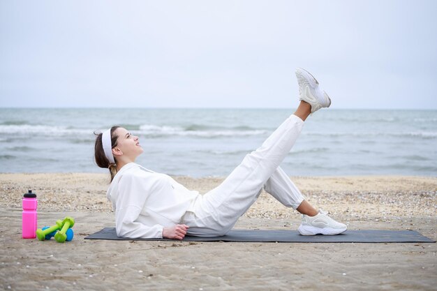 Das junge schöne Mädchen, das auf der Yogamatte liegt und ihr Bein hochhebt Foto in hoher Qualität