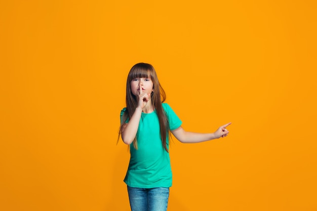 Das junge Teenager-Mädchen flüstert ein Geheimnis hinter ihrer Hand über den orangefarbenen Raum