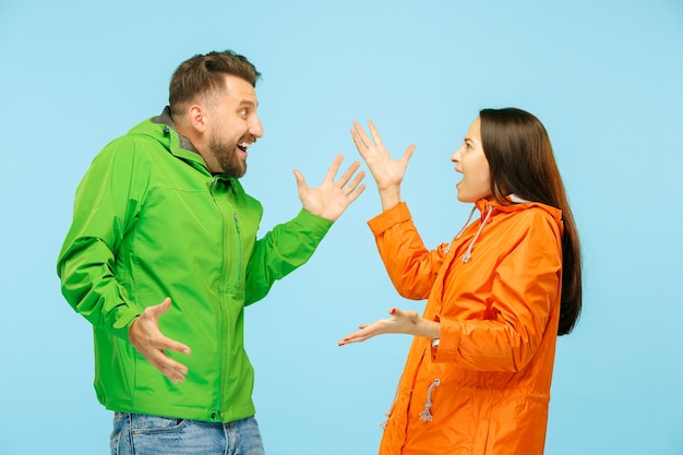 Das junge überraschte Paar im Studio in Herbstjacken isoliert auf blau. Menschliche negative Emotionen. Konzept des kalten Wetters. Weibliche und männliche Modekonzepte