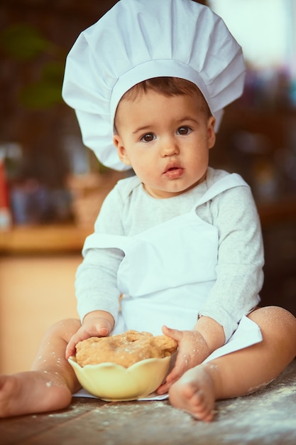 Das kleine Baby, das auf dem Tisch sitzt und mit Teig spielt