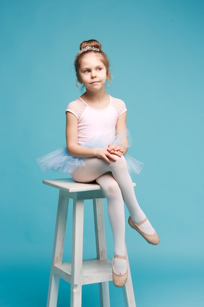 Das kleine Mädchen als Balerina-Tänzerin sitzt auf weißem Holzstuhl im blauen Studio