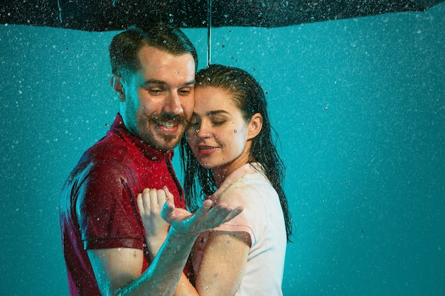 Das liebende Paar im Regen mit Regenschirm auf einem türkisfarbenen Hintergrund