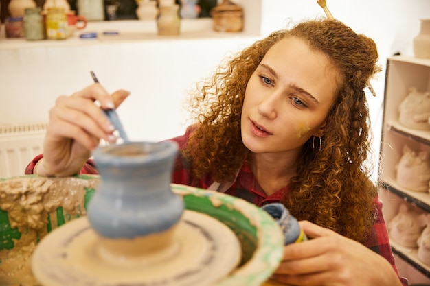 Das lockige rothaarige Mädchen konzentriert sich darauf, vor dem Backen eine Keramikvase abzudecken