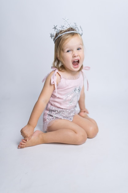 Das lustige kleine Mädchen, das wie eine Prinzessin gekleidet wird, sitzt im Studio