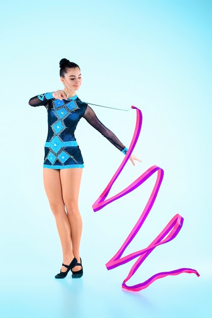Das Mädchen, das Gymnastik tanzt, tanzt mit farbigem Band auf einem blauen Hintergrund