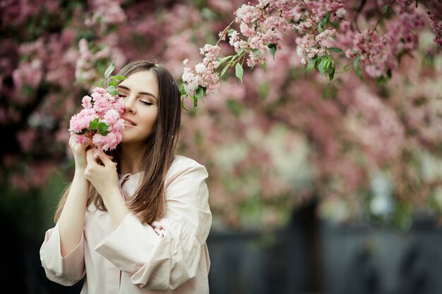 Das Mädchen, das ihre Augen schließt, lächelt und hält einen Kirschblüte-Zweig