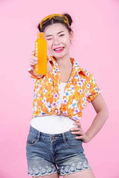 Das Mädchen hält eine Flasche Orangensaft auf einem rosa Hintergrund.