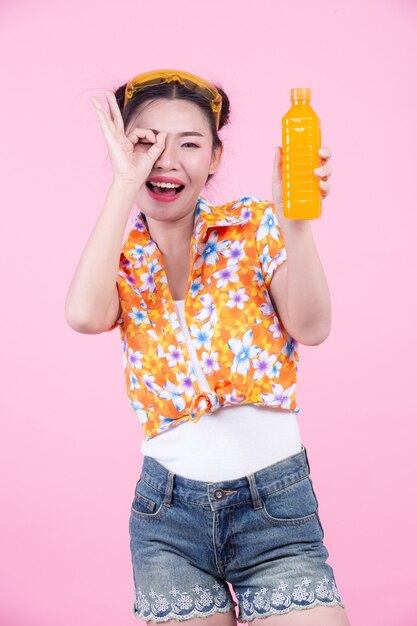 Das Mädchen hält eine Flasche Orangensaft auf einem rosa Hintergrund.