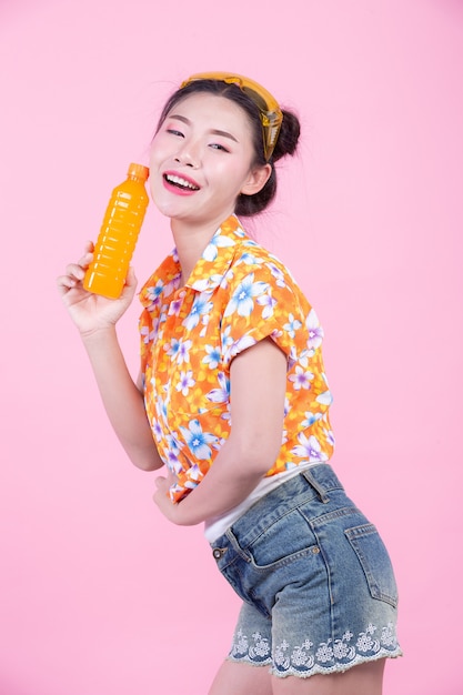 Das Mädchen hält eine Flasche Orangensaft auf einem rosa Hintergrund.