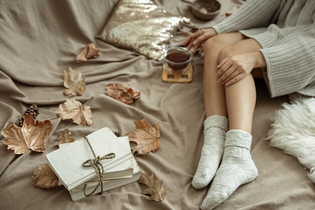 Das Mädchen liegt mit einer Tasse Tee in warmen Socken im Bett, Herbststimmung, Komfort.