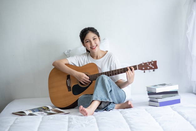 Das Mädchen saß und spielte Gitarre auf dem Bett.