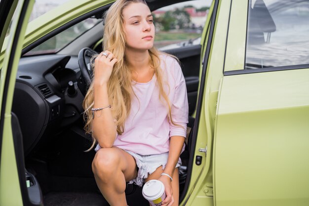 das Mädchen sitzt im Auto und trinkt Kaffee