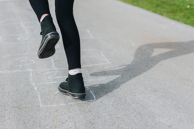 Das Mädchen springend in die Kreidekästen, die auf Asphalt gezeichnet werden