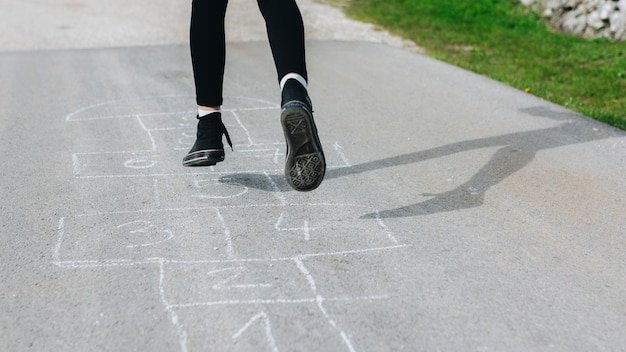 Das Mädchen springend in die Kreidekästen, die auf Asphalt gezeichnet werden