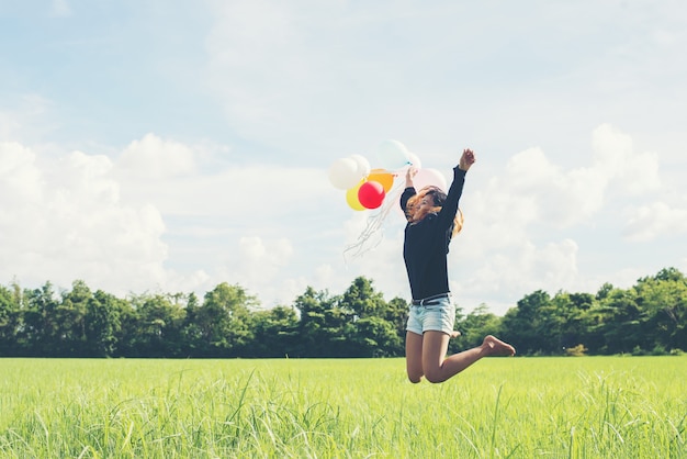 Das Mädchen springend mit Ballonen auf dem grünen Wiese