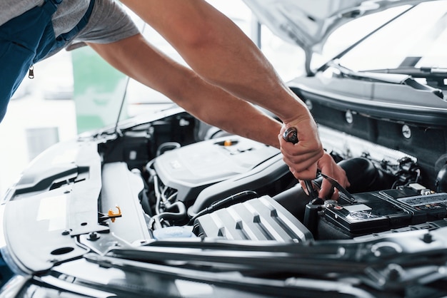 Das muss aufgeladen werden. Reparatur des Autos nach einem Unfall. Mann, der mit Motor unter der Haube arbeitet