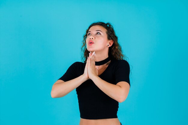 Das nachschlagende Mädchen betet, indem es die Hände auf blauem Hintergrund zusammenhält