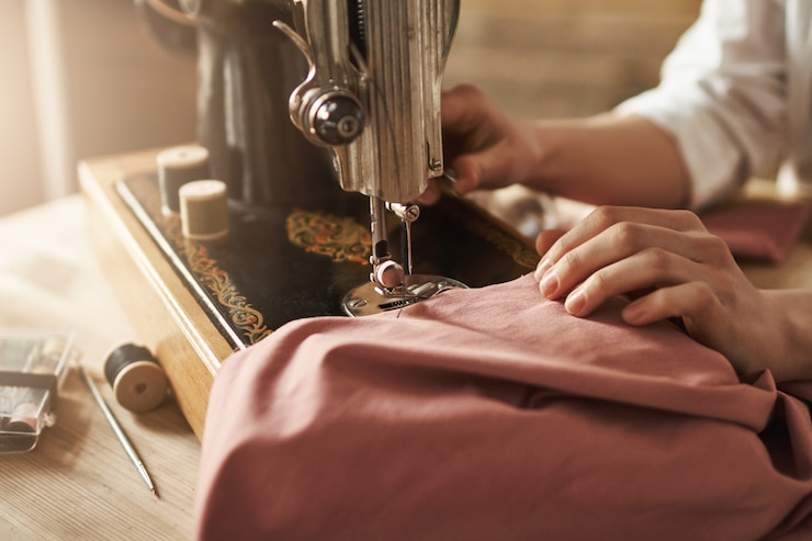 Kostenlose Foto das nähen hält meinen geist entspannt. beschnittener schuss der schneiderin, die an neuem projekt arbeitet, kleidung mit nähmaschine in der werkstatt macht, beschäftigt ist. junge designerin, die ihre ideen wahr werden lässt