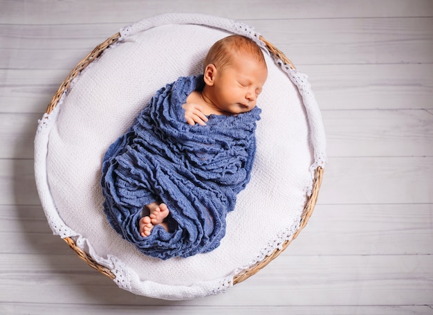 Das neugeborene Baby, das im blauen Schal eingehüllt wird, schläft auf weißem Kissen