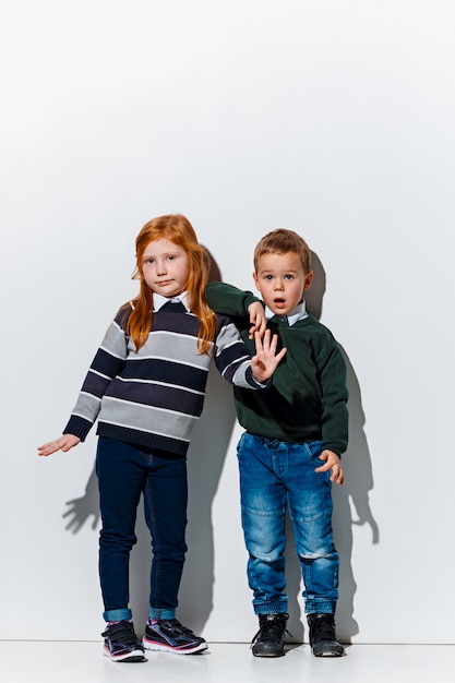 Das Porträt des niedlichen kleinen Jungen und des Mädchens in der stilvollen Jeanskleidung, die aufwirft