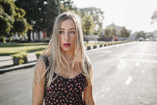 Das Porträt einer sexy blonden jungen Frau mit täglichem Make-up steht mitten auf der Straße
