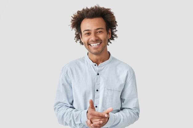 Das Porträt eines fröhlichen gutaussehenden Mannes hält die Hände zusammen, lächelt breit und trägt ein elegantes Hemd