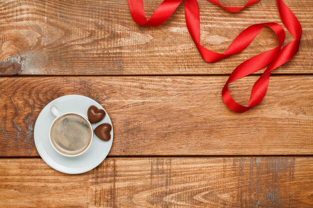 Das rote Band, kleine Herzen auf hölzernem Hintergrund mit einer Tasse Kaffee