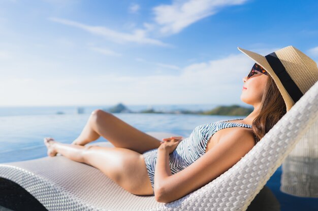 Das schöne junge asiatische Frauenlächeln des Porträts, das glücklich ist, entspannen sich um Swimmingpool im Hotelerholungsort für Freizeit