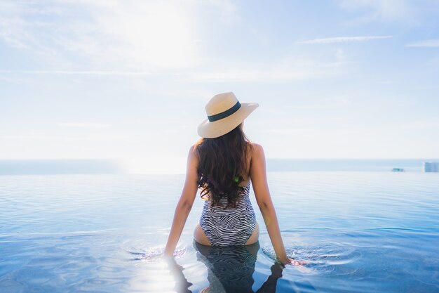 Das schöne junge asiatische Frauenlächeln des Porträts, das glücklich ist, entspannen sich um Swimmingpool im Hotelerholungsort für Freizeit