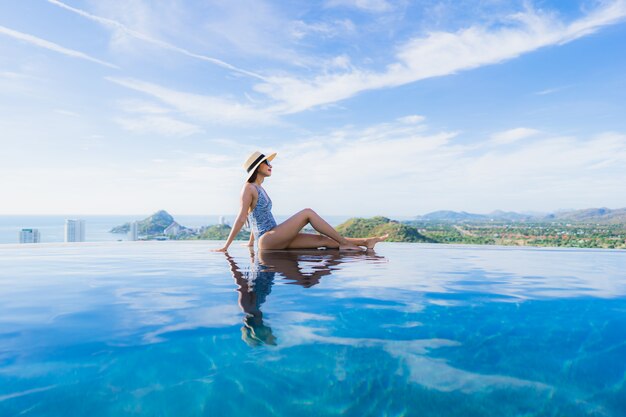 Das schöne junge asiatische Frauenlächeln des Porträts, das glücklich ist, entspannen sich um Swimmingpool im Hotelerholungsort für Freizeit