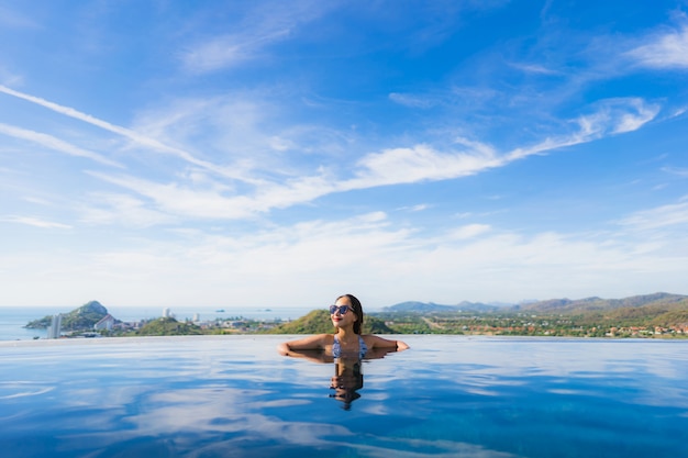 Das schöne junge asiatische Frauenlächeln des Porträts, das glücklich ist, entspannen sich um Swimmingpool im Hotelerholungsort für Freizeit