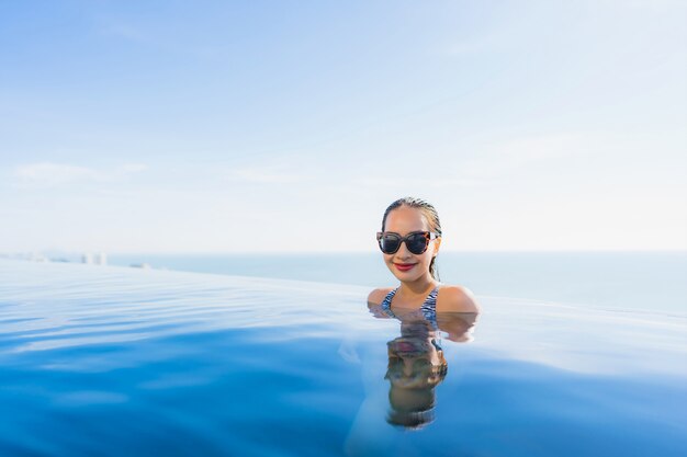 Das schöne junge asiatische Frauenlächeln des Porträts, das glücklich ist, entspannen sich um Swimmingpool im Hotelerholungsort für Freizeit