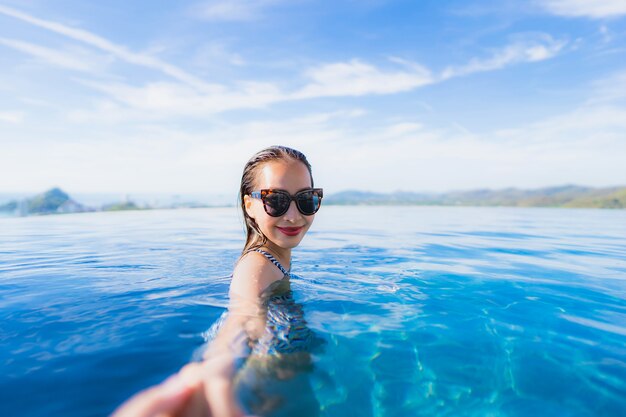 Das schöne junge asiatische Frauenlächeln des Porträts, das glücklich ist, entspannen sich um Swimmingpool im Hotelerholungsort für Freizeit