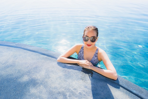 Das schöne junge asiatische Frauenlächeln des Porträts, das glücklich ist, entspannen sich um Swimmingpool im Hotelerholungsort für Freizeit