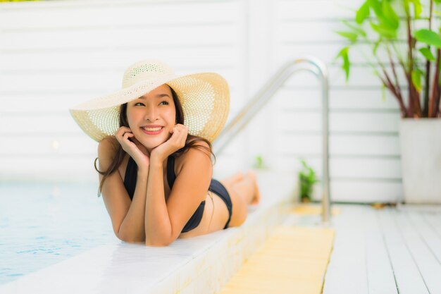 Das schöne junge asiatische Frauenlächeln des Porträts, das glücklich ist, entspannen sich um Swimmingpool im Hotelerholungsort für Freizeit