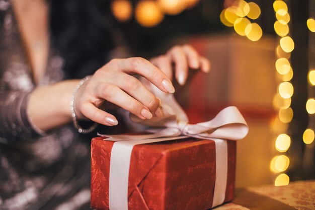 Das schöne Mädchen sitzt auf dem Boden und öffnet ein Geschenk