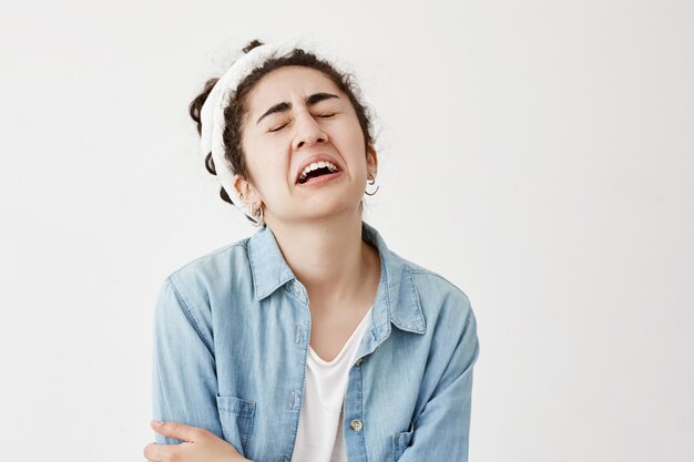 Das stressige, verwirrte junge weibliche Model mit dem dunklen, welligen Haar trägt einen Lappen und ein Jeanshemd, die in Panik sind, da es nicht weiß, was es mit einem Freund, einem besorgten, stirnrunzelnden Gesicht und Weinen anziehen soll.