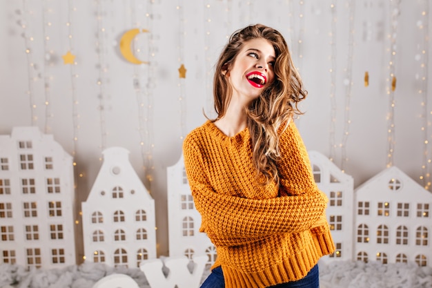 Das süße Model lacht aufrichtig in warmer Atmosphäre. Schöne Landschaft im Zimmer macht Mädchen glücklich