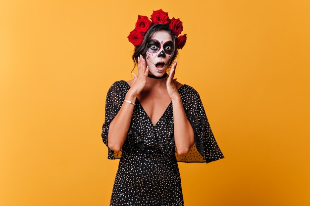 Das verängstigte Mädchen in der Halloween-Maske öffnete überrascht den Mund. Porträt der Frau im gepunkteten Kleid an der isolierten Wand.