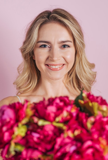 Defocused Blumenblumenstrauß vor lächelnder junger Frau gegen rosa Hintergrund