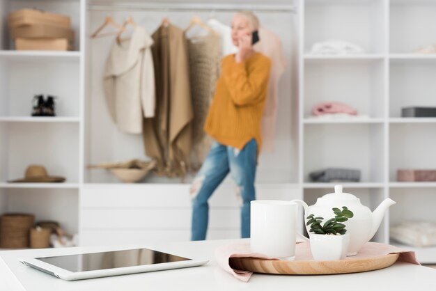 Defocused reife Frau, die am Telefon mit Tabletten- und Teesatz spricht