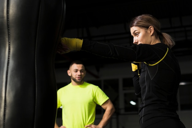 Defocused Trainer, der weiblichen Boxer aufpasst, auf Sandsack zu üben