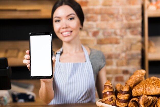 Defocused weiblicher Bäcker, der hinter dem Zähler zeigt Handy steht