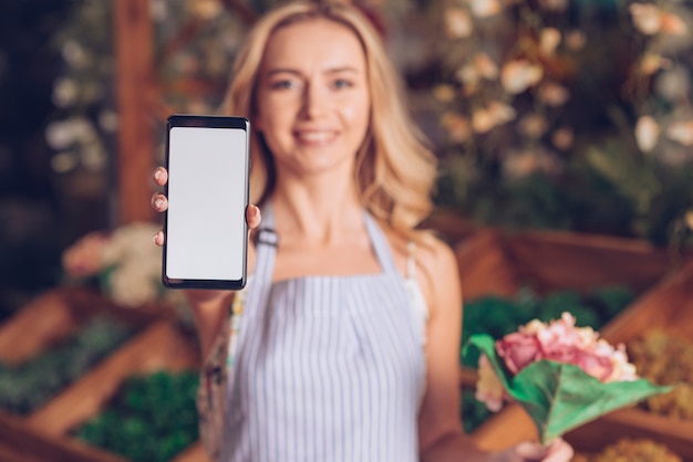 Defocused weiblicher Florist, der in der Hand die Blume zeigt intelligentes Telefon mit weißer Bildschirmanzeige hält