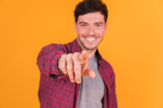 Kostenloses Foto defocussed junger mann, der seinen finger in richtung zur kamera gegen farbigen hintergrund zeigt