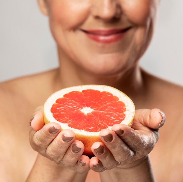 Defokussierte ältere Smiley-Frau, die die Hälfte der Grapefruit in ihren Händen hält
