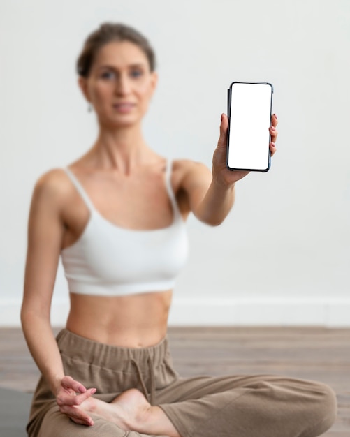 Defokussierte Frau zu Hause, die Yoga macht und Smartphone hält