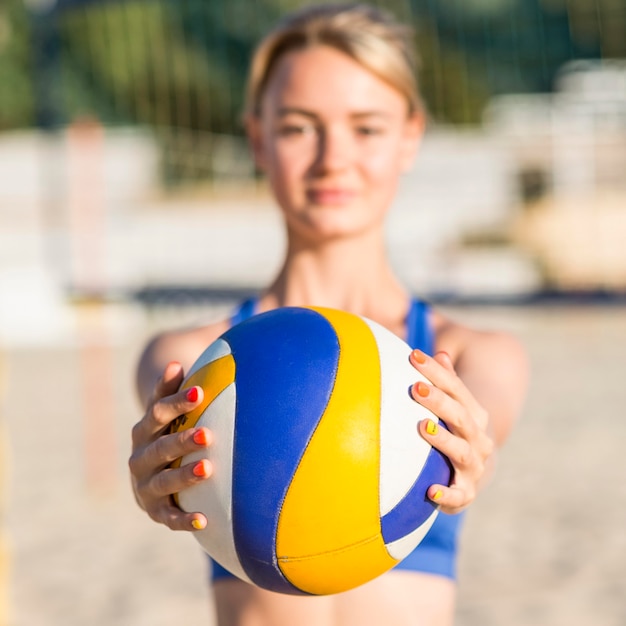 Defokussierte Volleyballspielerin am Strand, die Ball hält