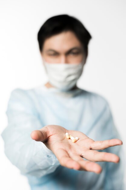Defokussierter Arzt mit medizinischer Maske, die Pillen in der Hand hält