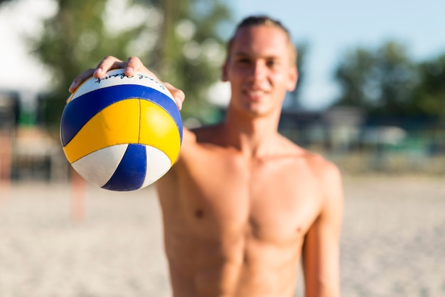 Defokussierter hemdloser männlicher Volleyballspieler am Strand, der Ball hält